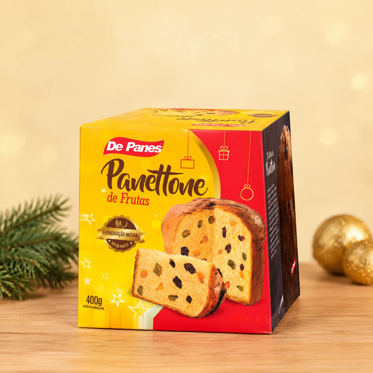 Caixa de Panettone de Frutas De Panes sobre mesa com ramo de pinheiro e bolas de Natal