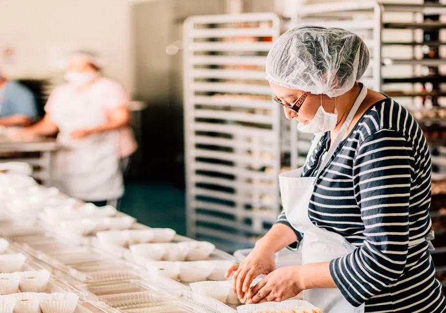 Funcionária com touca e máscara modelando pães